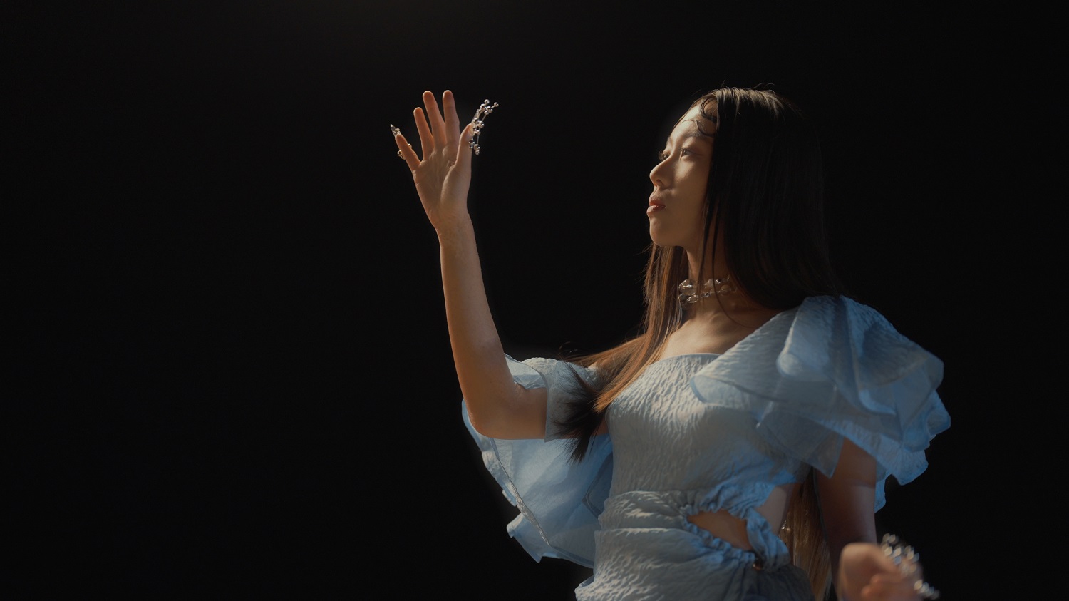 XTIE wearing a blue dress with a black background. Hand in the air.